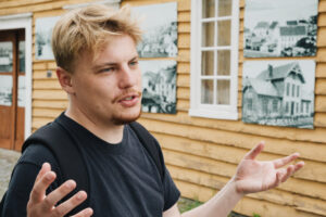 Young man explaining in front of a wall of photos.